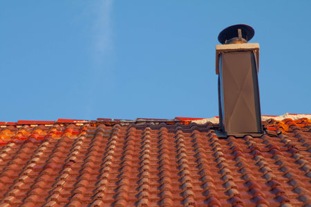 A rooftop with tiles and a chimney against a blue sky backgroundの写真素材
