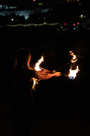 A vertical shot of a female fire dancer in the darkness.