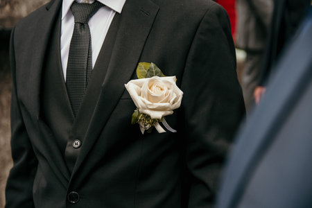 Close-up cropped image groom wearing dark suit with white rose on wedding day.