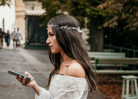 Candid photo of bride wearing white wedding dress holding mobile phone.