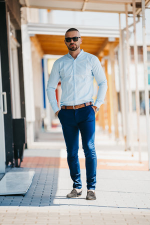 A cool handsome Caucasian man wearing an elegant light blue shirt and sunglasses posing outdoorの写真素材