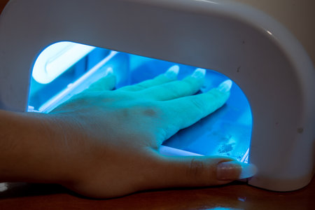 A female hand with manicured nails inside of UV lamp in a nail salonの写真素材