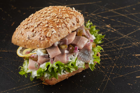 A closeup of a smoked fish sandwich on a black wooden surfaceの写真素材