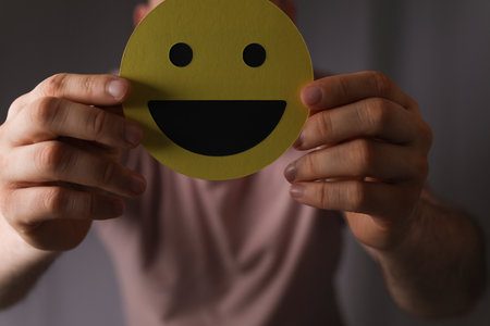 A closeup of a person holding a yellow smiley face in front of his face, business recruitmentの写真素材