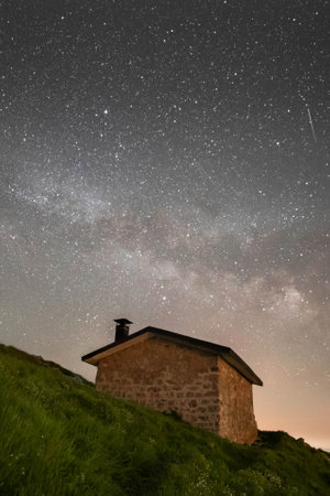 A vertical shot of a small house on a green hill with a starry night sky backgroundの写真素材