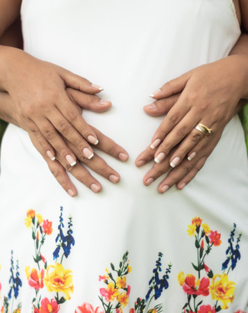 A vertical shot of a man hugging his pregnant wife wearing a floral dressの写真素材