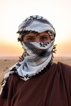 A portrait of a woman wearing a shemagh scarf against a desert landscapeの写真素材