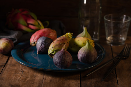 A closeup shot of a blue plate full of figs, prickly pears with dragon fruit, fork, knife and empty...