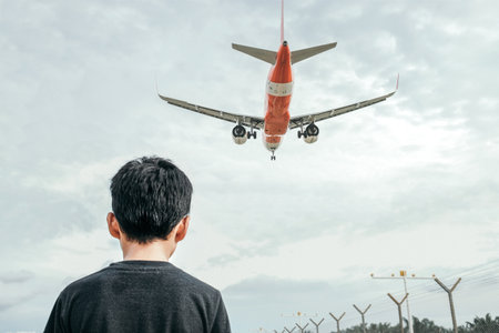 A shot of a little boy standing outdoors, with an orange bottom plane flying under a gloomy skyの写真素材