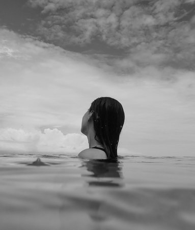 A grayscale shot of a brunette female swimming in the sea under a cloudy sky