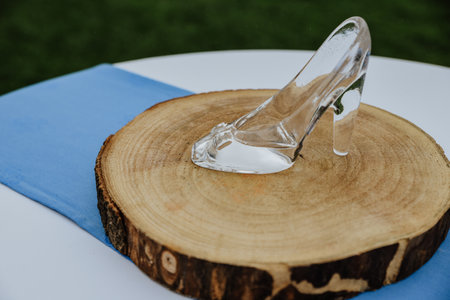 A closeup shot of a crystal slipper on a sliced wooden circle on a blue and white tableclothの写真素材
