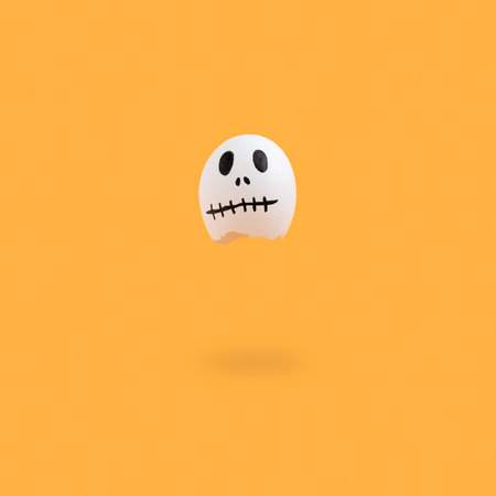 A Halloween background of an eggshell painted as a ghost character on an orange surfaceの写真素材