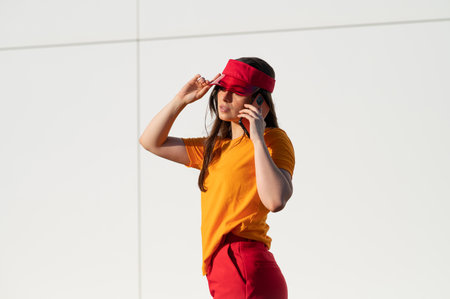 A stylish Caucasian female in an orange t-shirt and red cap talking on the phoneの写真素材
