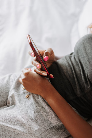 A closeup of a black female in casual clothes looking at her phone laying on the bedの写真素材