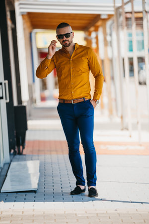 A cool handsome Caucasian man wearing an elegant mustard shirt and sunglasses posing outdoorの写真素材