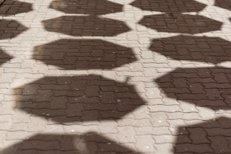 A close up shot of a ground in public has the shadows of the design of a wall on it