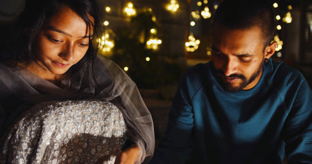 A beautiful young Indian couple preparing for Diwali celebration while sitting outside at nightの写真素材