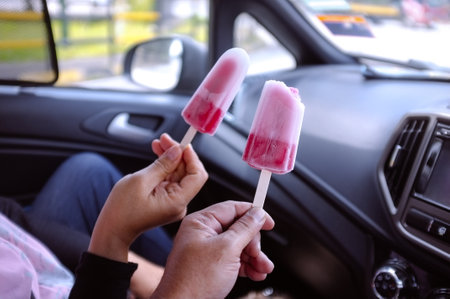 Two people holding pink ice cream sticks in the car