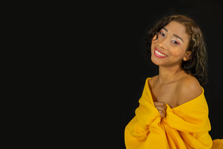 A sexy African American female wearing a yellow dress and posing on the black backgroundの写真素材