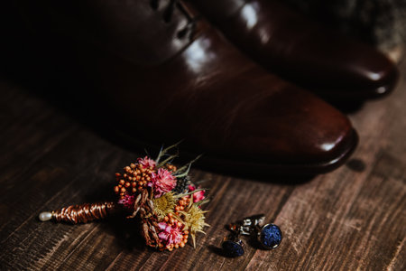 A closeup of the groom accessories - sleek cufflinks and a small bouquet pin, near brown shoes
