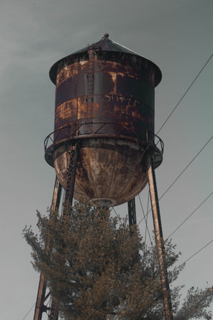 A vertical shot of an old and dirty liquid container on a metal tower outdoorsの写真素材