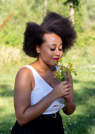 An African American female smelling the yellow wildflowers while on picnic at Tormes River in Salamanca City, Spainの写真素材