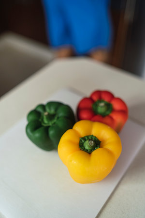 A vertical high angle closeup shallow focus of three bell peppers on a board