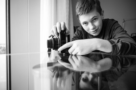 A grayscale shot of a Caucasian boy practicing how to use his camera at homeの写真素材