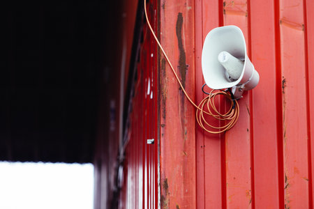 A white horn loudspeaker mounted on the building's red wallの写真素材