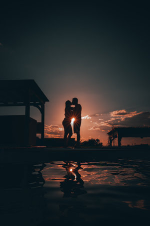 The silhouette of a romantic couple kissing against a sunset skyの写真素材