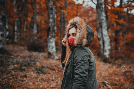 A beautiful caucasian female in a red mask posing in an autumn forestの写真素材