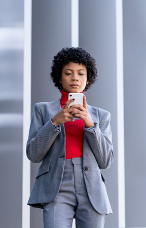 A young African-American businesswoman texting on the phone in a business building