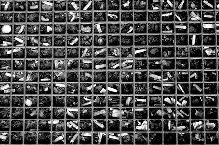 A top view of wire mesh with dozens of cigarette butts scattered in it - pollution concept