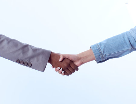 A close-up shot of handshaking of black and white businesswomen isolated on a white backgroundの写真素材