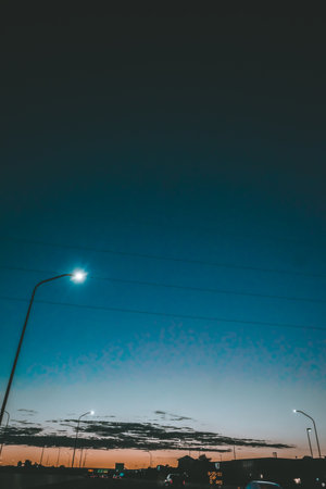 A vertical shot of a sunset scene with lamppost silhouettes anddark cloudsの写真素材