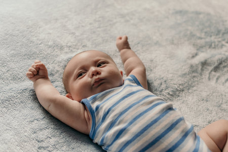 A cute Caucasian toddler on a bed with blue-white striped clothesの写真素材