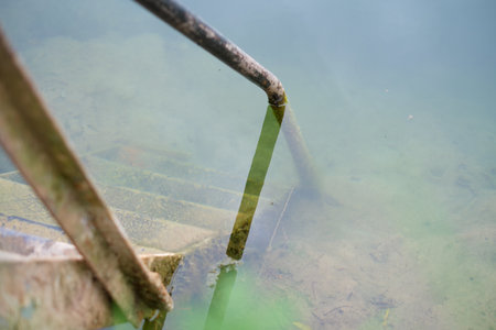 Selective focus shot of a rural metal ladder that leads into a cold quarry lake, shot on a cloudy day. Bathing in old gravel mining grounds.の写真素材