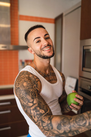 A vertical shot of a tattooed Caucasian male athlete taking an apple out of a fridgeの写真素材