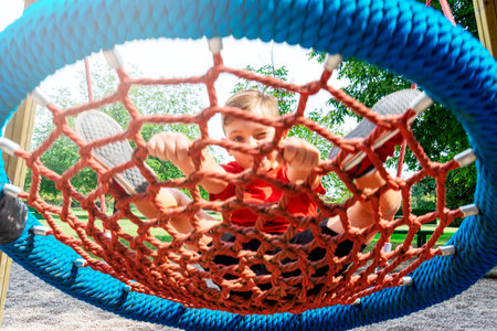 A Caucasian child playing in a park playground wearing red t-shirt on a  bright sunny dayの写真素材
