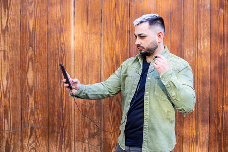 A young man waiting at the bus stop with his phone in his hand during a video callの写真素材