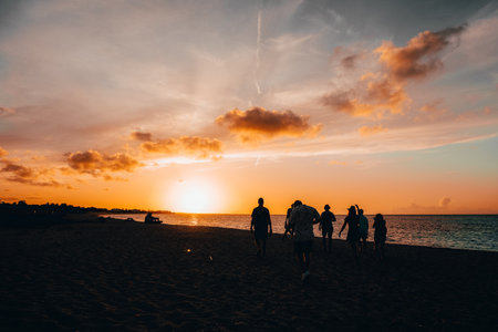 A silhouette of tourists enjoying the beach during a beautiful sunsetの写真素材