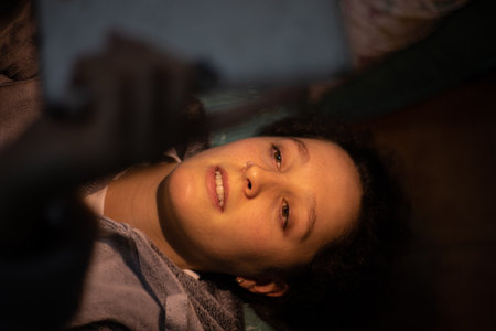 A closeup of a young woman lying in bed and looking at the tablet.