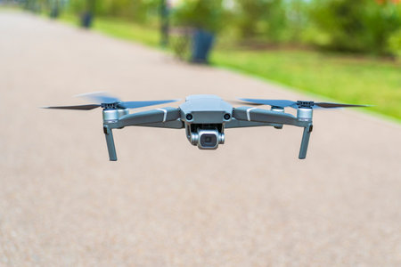 A small quadrocopter with a camera is hovering in the air in a public park and filming.