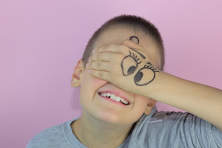 A cheerful Caucasian boy covering his face with his hand with a silly eye drawingの写真素材