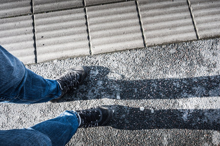 A vertical shot of male feet with jeans and sports shoes standing outdoors on a sunny day