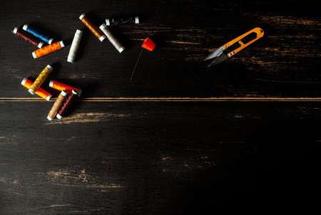 A top view of colorful threads, needle, thimble, and nippers on an old wooden backgroundの写真素材