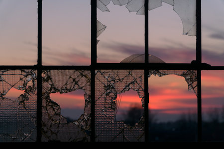 A window with broken glasses and a colorful sunset on a backgroundの写真素材