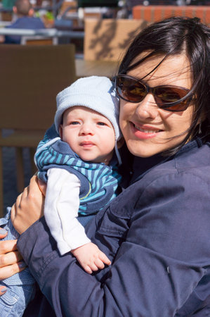 A woman with sunglasses holding her baby in the cafeの写真素材