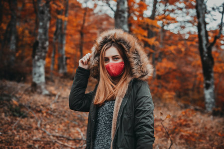 A beautiful caucasian female in a red mask posing in an autumn forestの写真素材