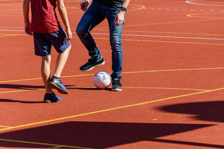 Low section photo of father and son playing soccer or football on orange sports court outdoorの写真素材